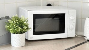 A white microwave oven with a digital display and control panel, placed on a kitchen counter next to a white pot with green plants. - Seaside Serenity Retreat in Wallasey (Wallasey)