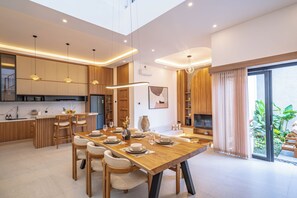 Une cuisine moderne avec des meubles en bois, un coin repas doté d’une grande table et un téléviseur dans le salon.