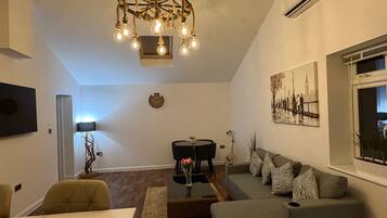 A modern living room with a chandelier, a sofa, a dining table, and a painting on the wall.