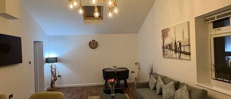 A modern living room with a chandelier, a sofa, a dining table, and a painting on the wall.