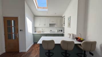 A modern kitchen with a skylight, a wooden door, and a bar area with three stools.