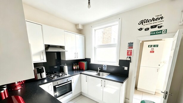 A modern kitchen with white cabinets, a black countertop, and a window providing natural light. - South East London 5-Bed House, Sleeps 7 Foresthill (London)