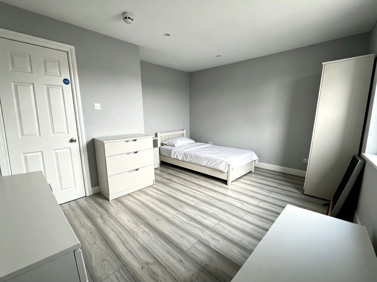 A bedroom with a bed, a dresser, a wardrobe, and a door.