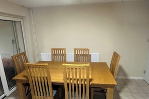 A dining area with a wooden table and chairs, a radiator, and a sliding glass door. - Spacious 6 Bedroom Home for Families&Contractors (Hornchurch)