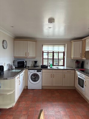A kitchen with a washing machine, microwave, sink, and cabinets. - Lookout Porthpean Cottage Sleeps 5 - Golf (St Austell)