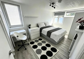 Un dormitorio con cama, mesita de noche, silla y ventana.