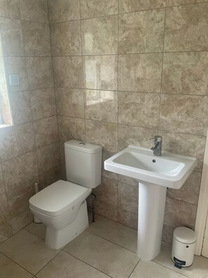 A bathroom with a toilet, sink, and trash bin. - Cosy 2 Bed Apartment in Enfield (Enfield)