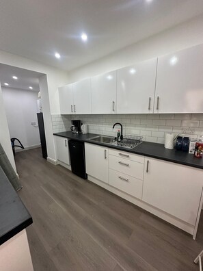 A modern kitchen with white cabinets, a black countertop, and a dishwasher. - Private Bedroom with kitchen Access (London)