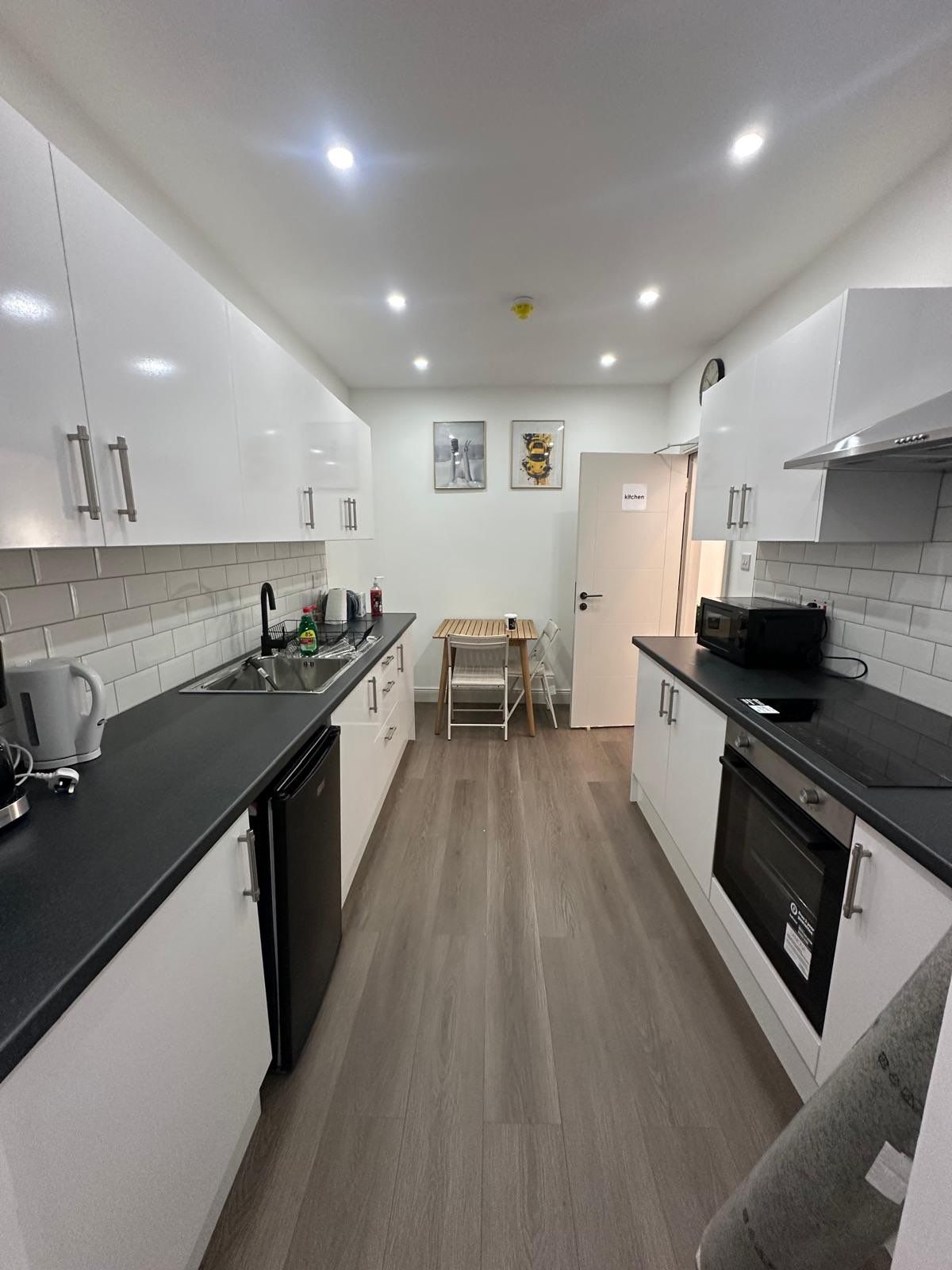 A modern kitchen with white cabinets, a black countertop, and a wooden floor.
