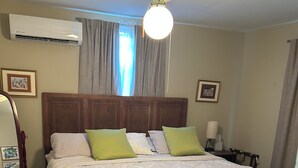 Hotellihuone, jossa on sänky, kattotuuletin, ilmastointilaite, yöpöytä lampulla ja kukkapainatuksin koristeltu rahi.