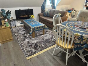 A living room with a sofa, a dining table with chairs, a TV, and a patterned rug. - Apartment Sleeps 4 with Parking (Rye)