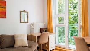 Ett rum med en soffa, ett skrivbord, en stol, ett element och ett fönster med gardiner.