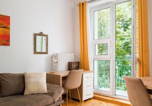 Una habitación con sofá, escritorio, silla, radiador y ventana con cortinas.