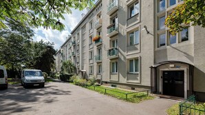 En flervåningsbostadsbyggnad med balkonger, en asfalterad uppfart och en parkerad bil på gatan.