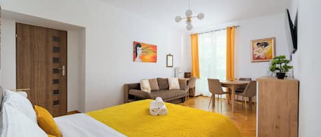 A modern hotel room with a bed, a desk, a sofa, and a dining area.