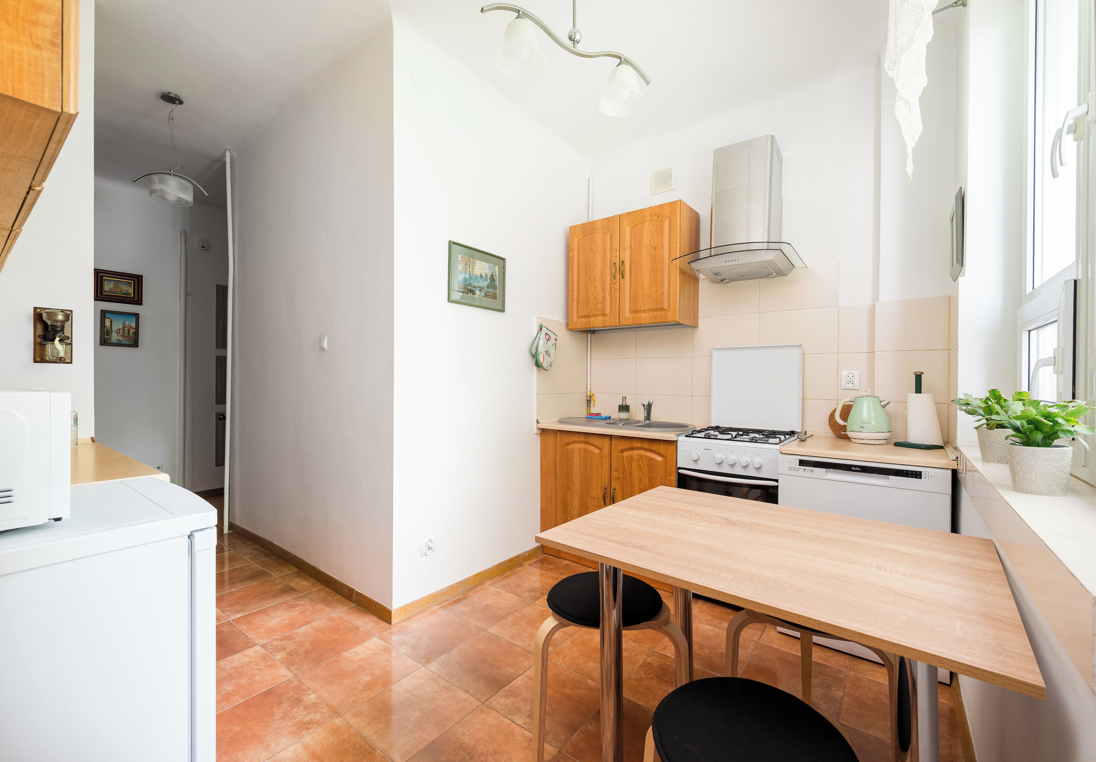 A compact kitchen with wooden cabinets, a gas stove, a dishwasher, and a small dining table with two chairs.