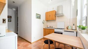 A compact kitchen with wooden cabinets, a gas stove, a dishwasher, and a small dining table with two chairs.