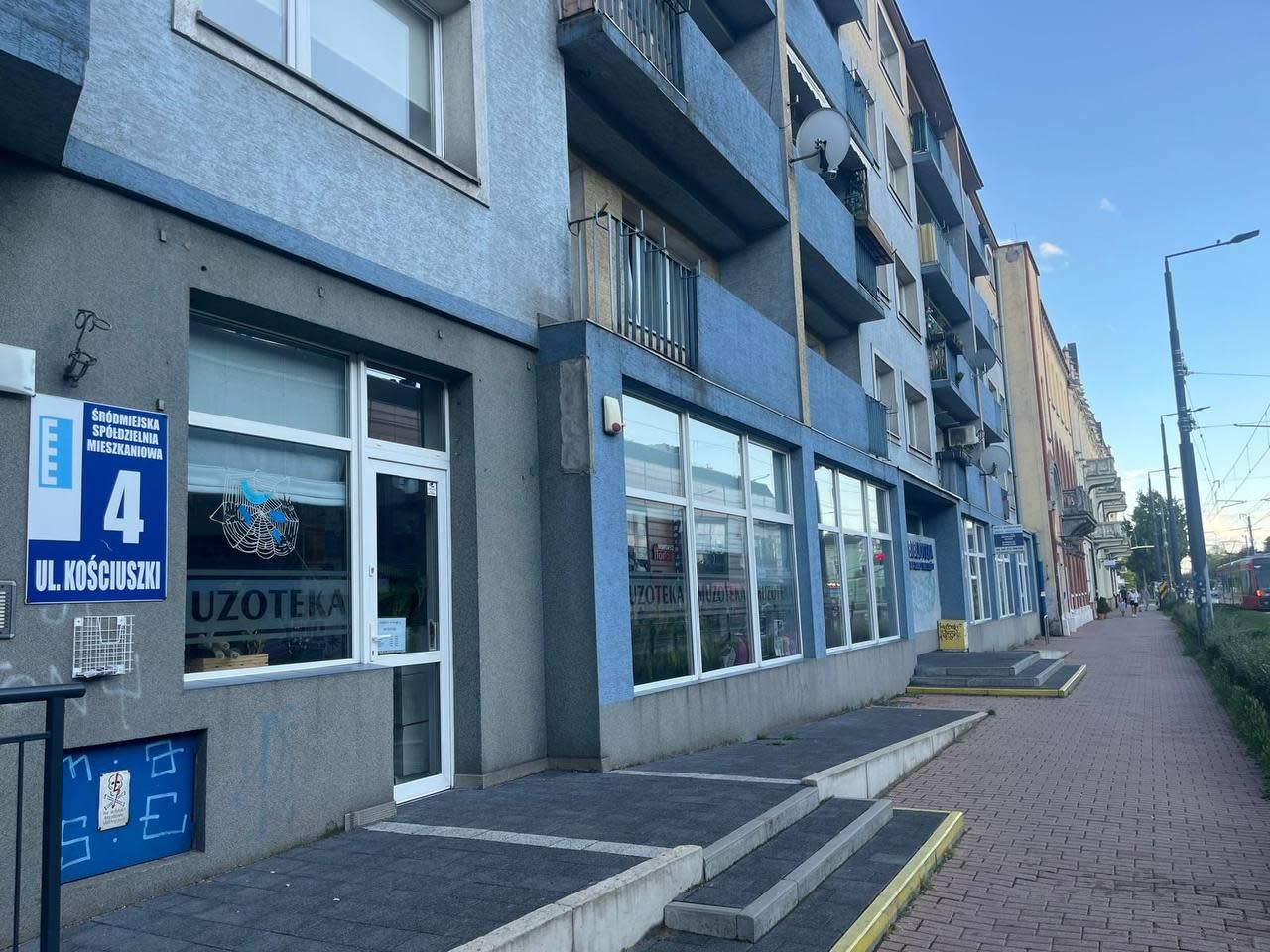 Ein Gebäude mit einer Schaufensterfront, auf der 'UZOTEKA' steht, und einem Schild, das den 4. Stock anzeigt.