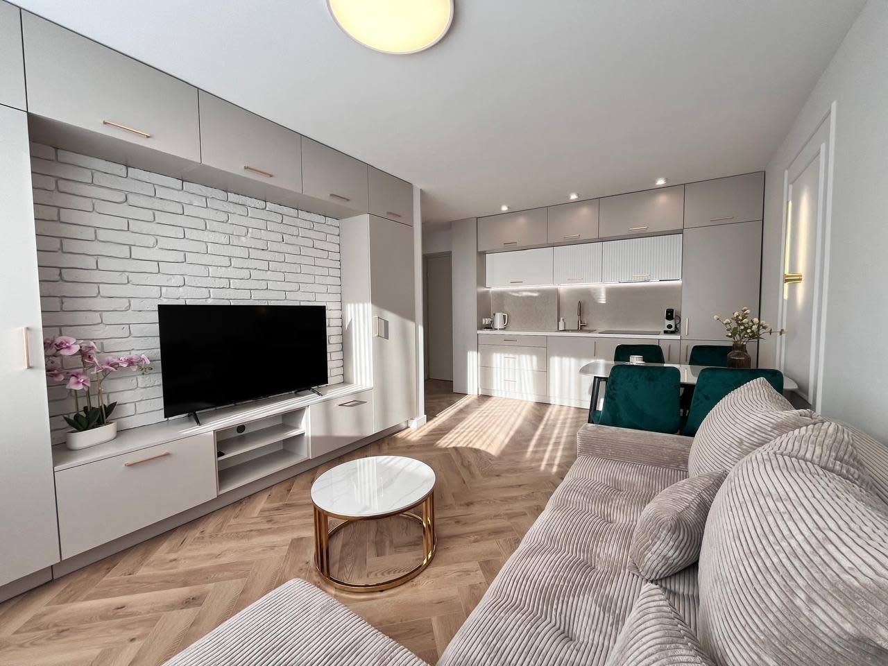 Un salon moderne avec un téléviseur à écran plat, un canapé, une table basse et un coin cuisine à l’arrière-plan.