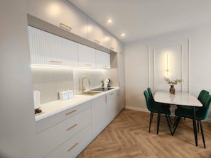 A modern kitchen with white cabinetry, a built-in sink, and a dining area with a white table and green chairs.