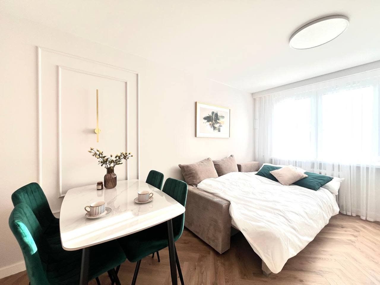 A modern bedroom with a bed, bedside table, and a dining area with chairs.