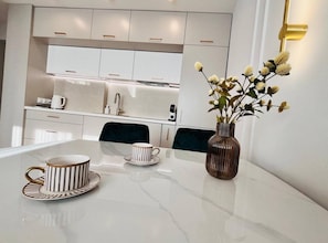 A modern kitchen with white cabinets, a stainless steel sink, and a dining table with a vase of flowers.