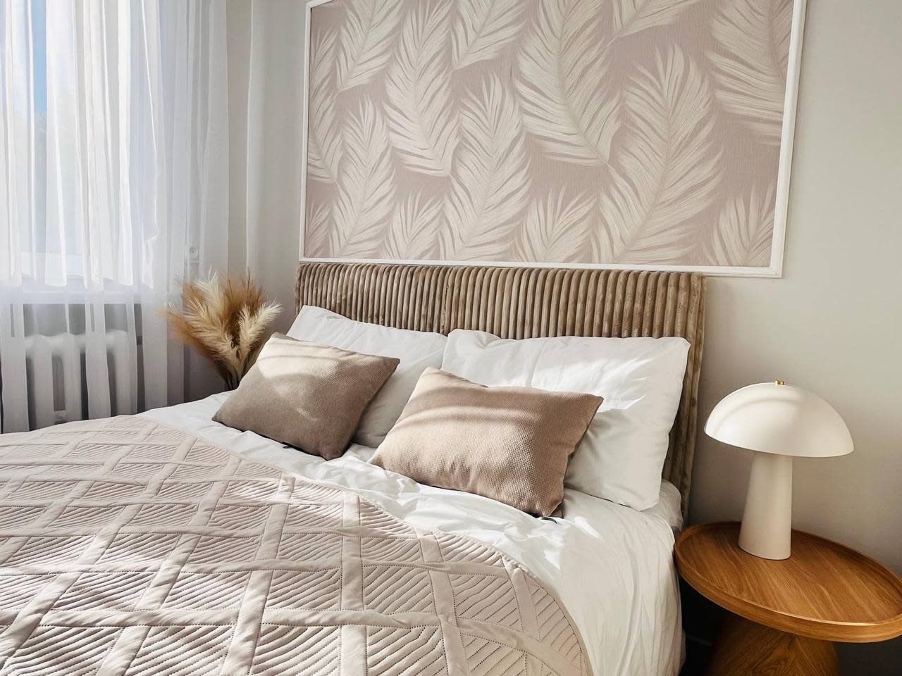 A neatly made bed with a patterned bedspread, two pillows, a bedside lamp, and a wall-mounted artwork.