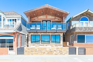 A two-story building with a stone facade, large windows, and a balcony. - Coveted Beachfront Home with Oceanfront Patio and Balcony (Newport Beach)