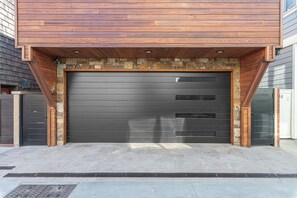 Eine moderne Garage mit einer dunkelgrauen Tür, Holzelementen und einer Wand aus Naturstein.