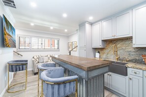A modern kitchen with a marble backsplash, light-colored cabinets, and a bar area with stools. - Coveted Beachfront Home with Oceanfront Patio and Balcony (Newport Beach)