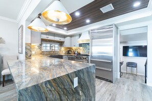 A modern kitchen with a marble island, stainless steel appliances, and pendant lighting. - Coveted Beachfront Home with Oceanfront Patio and Balcony (Newport Beach)