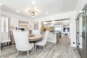 A dining area with a round table, two upholstered chairs, a chandelier, and a kitchen in the background. - Coveted Beachfront Home with Oceanfront Patio and Balcony (Newport Beach)