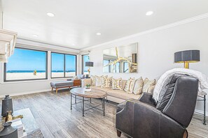 A spacious living room with a large window overlooking a beach, a sofa, a coffee table, and a lamp. - Coveted Beachfront Home with Oceanfront Patio and Balcony (Newport Beach)
