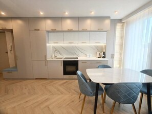 A modern kitchen with built-in appliances, a dining area with a table and chairs, and a wooden floor.