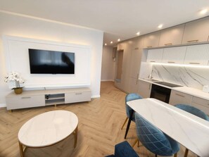 A modern living room with a flat-screen TV, a dining area with a marble table, and a kitchen with a marble countertop.
