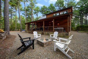 A cabin with a fire pit and Adirondack chairs in a forest setting.