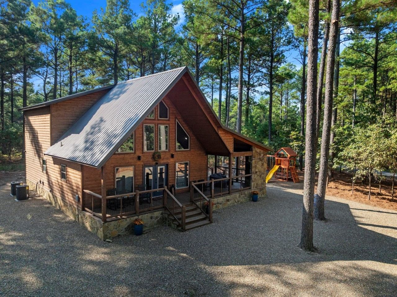 A cabin with a sloped roof, a porch, and a play area in a wooded setting.
