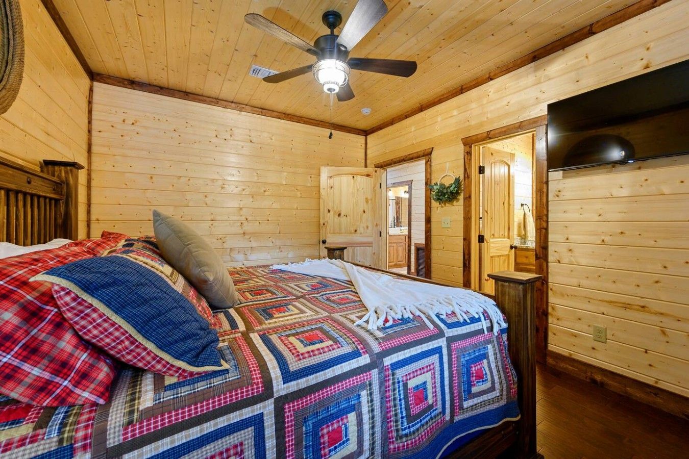 A wooden cabin room with a bed, a ceiling fan, and a kitchenette.