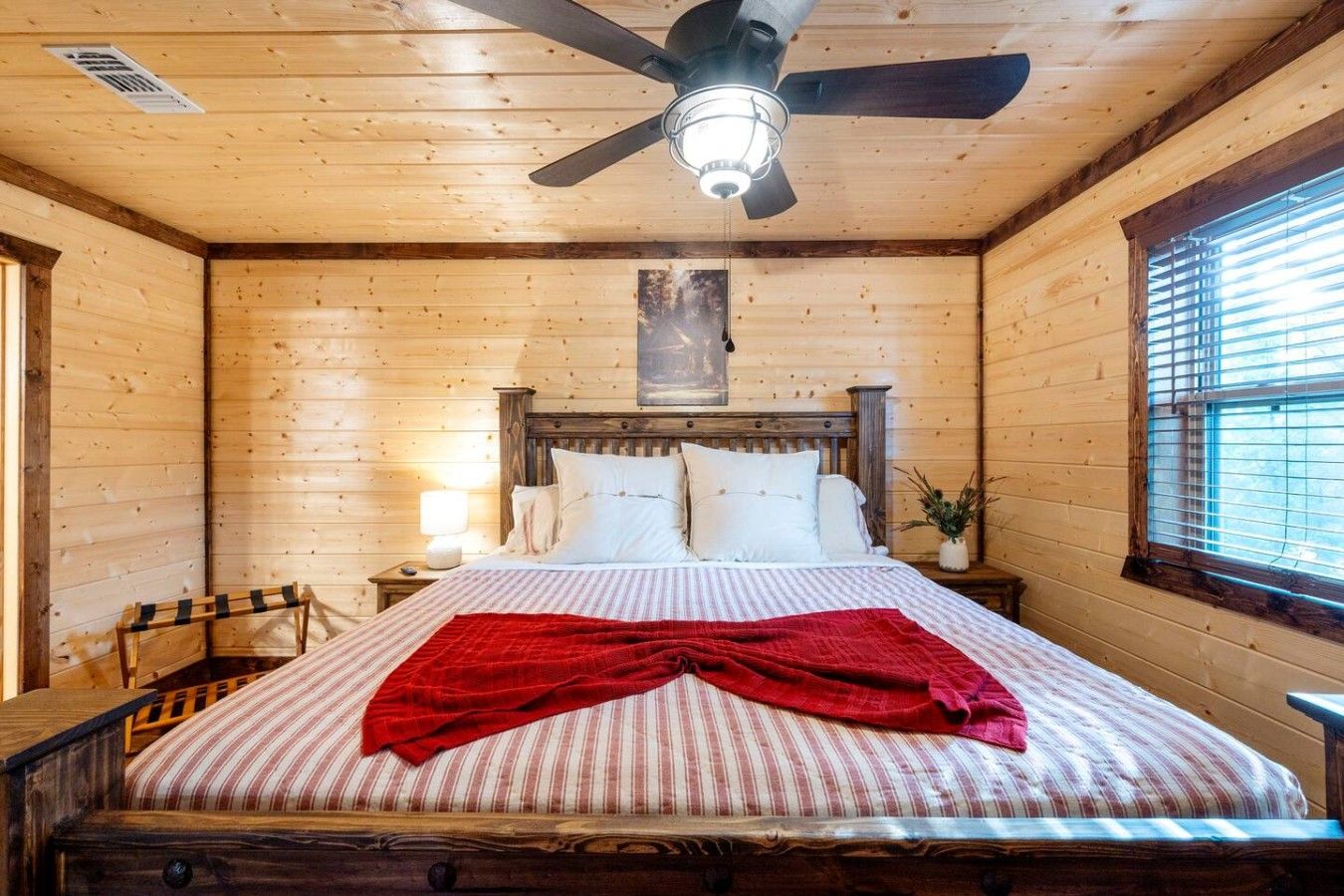 A wooden room with a bed, a nightstand, a chair, a ceiling fan, and a window.