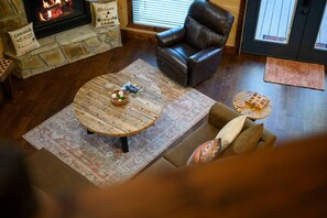A cozy living room with a stone fireplace, leather armchair, round coffee table, and a patterned rug. - Relax in the woods at Silverado! (Broken Bow)