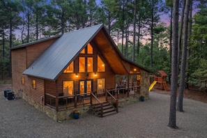 A log cabin with a porch, large windows, and a slide for children.