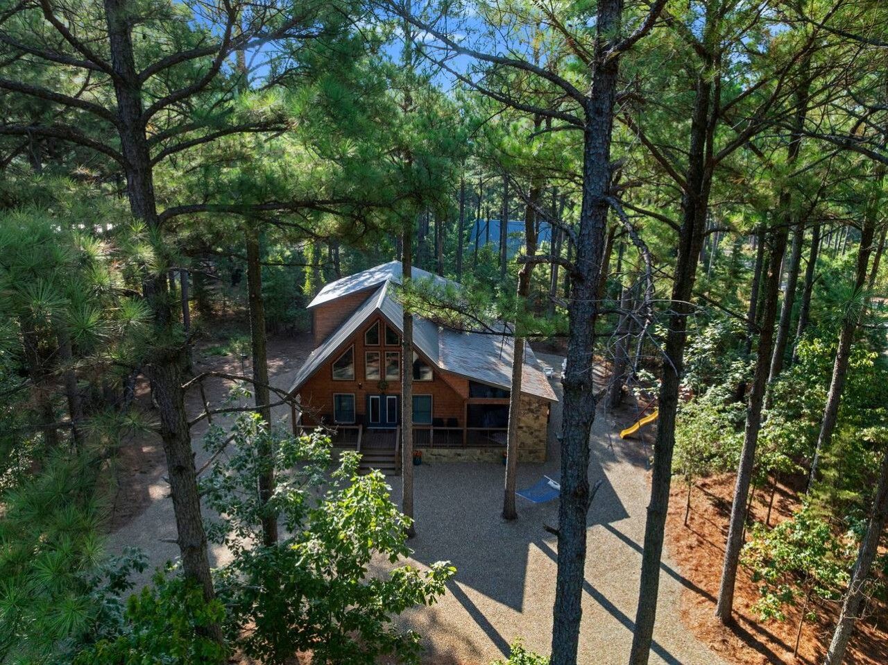 A cabin surrounded by dense forest, with a gravel driveway leading to the entrance.