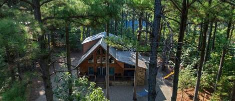 A cabin surrounded by dense forest, with a gravel driveway leading to the entrance.