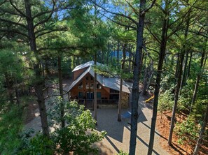 A cabin surrounded by dense forest, with a gravel driveway leading to the entrance.