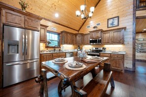 A spacious kitchen with wooden cabinets, stainless steel appliances, and a large dining table. - Relax in the woods at Silverado! (Broken Bow)