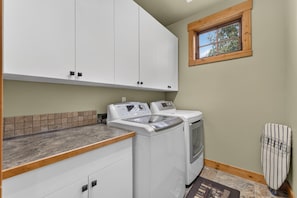 A laundry room with a washing machine and dryer, a window with a view of trees, and a tiled backsplash. - Big Dipper- Downtown Greystone by the lake with air conditioning (McCall)