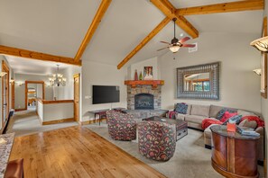 A spacious living room with a fireplace, wooden beams, a television, and a sofa. - Big Dipper- Downtown Greystone by the lake with air conditioning (McCall)