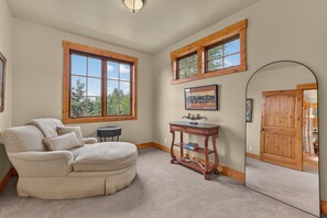 Une pièce avec une grande fenêtre, une porte en bois, une chaise ronde, une petite table et un miroir.