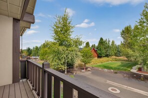 A wooden deck with a view of a road, trees, and a building in the distance. - Big Dipper- Downtown Greystone by the lake with air conditioning (McCall)