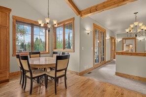A dining area with a wooden table and chairs, large windows, and a chandelier. - Big Dipper- Downtown Greystone by the lake with air conditioning (McCall)